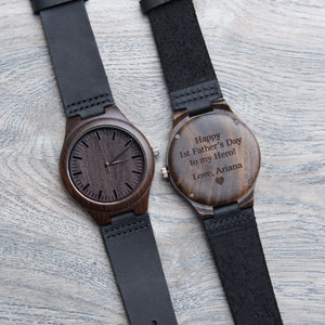Two wooden-finished wristwatches with black leather straps, one with a personalized father's day inscription on the back.